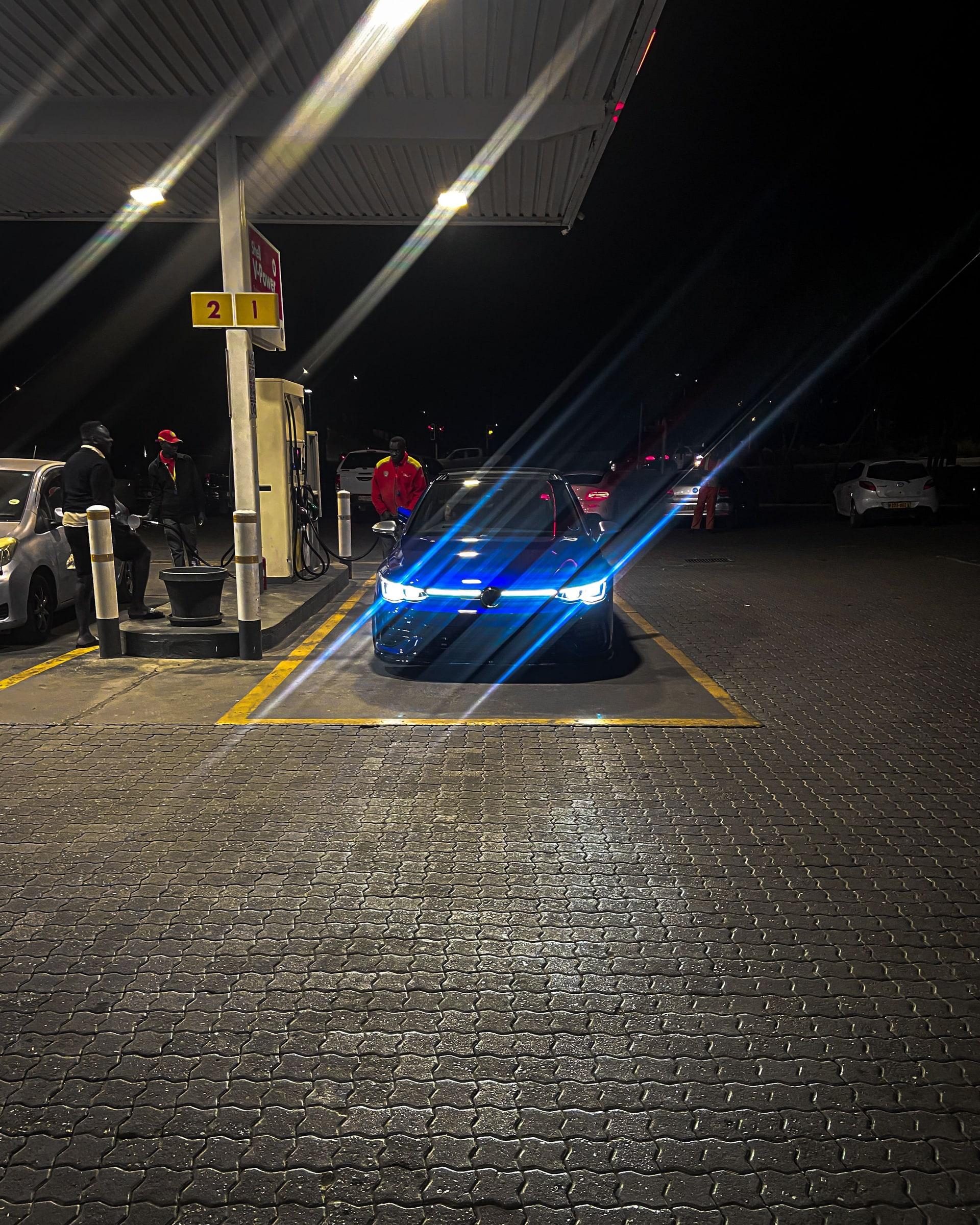 Hatchback with a blue light bar at a fuel station at night, light streaking across the frame