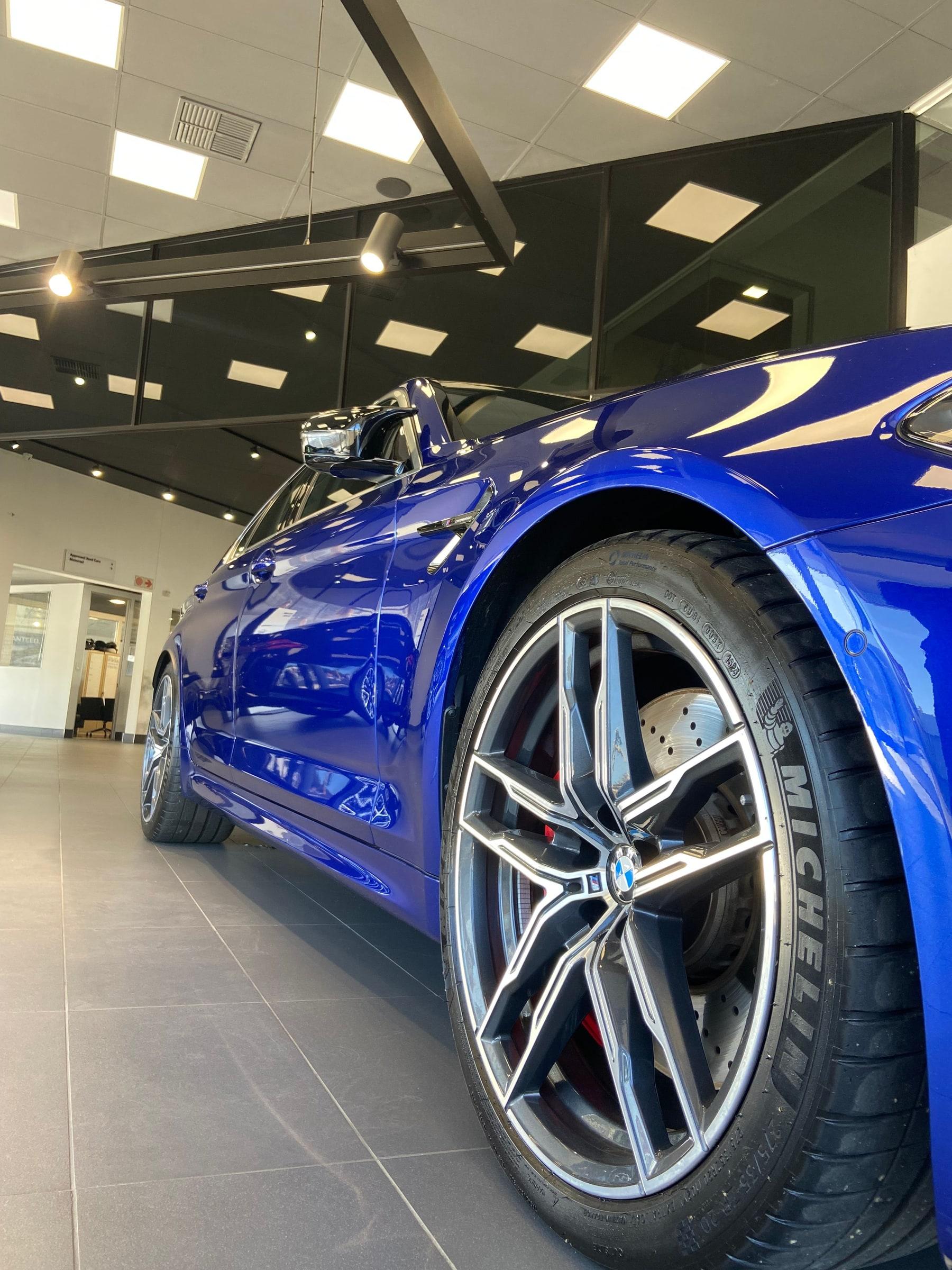 Front wheel and arch of a blue BMW M5 in a showroom